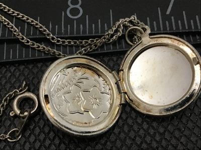 Sale Photo Thumbnail #50: A vintage oval locket pendant necklace featuring an etched floral motif on the front cover. The locket opens to reveal space for two small photos. Comes attached to a fine chain with a spring ring clasp. Shows light tarnishing and wear consistent with age