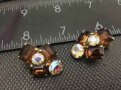 Sale Photo Thumbnail #130: Pair of vintage clip-on earrings featuring emerald-cut amber glass stones paired with sparkling round aurora borealis rhinestones in a gold-tone prong setting. Marked PAT. PEND. on the clip backs. Each earring measures approximately 1 inch in size. Good v