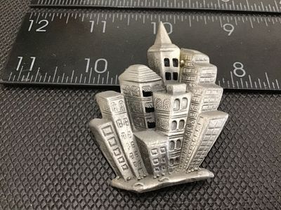 Sale Photo Thumbnail #74: A unique vintage pewter brooch by DAJO featuring a stylized, dimensional city skyline / cityscape with detailed architectural buildings. Signed DAJO on the back with a standard pin stem and rollover clasp. Measures approximately 2 inches tall by 2 inches 