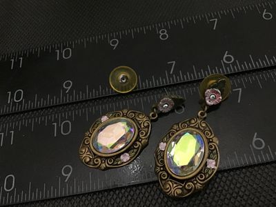 Sale Photo Thumbnail #84: Pair of vintage-style drop/dangle pierce-back earrings featuring an ornate brass-tone filigree metal frame, small floral accent detail with pink enamel, and large multifaceted iridescent aurora borealis rhinestones/glass stones. Measures approximately 2 i