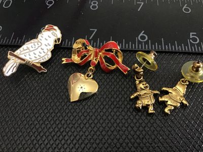 Sale Photo Thumbnail #231: A small collection of vintage fashion jewelry including an enamel parrot pin, a red enamel bow brooch with dangling heart charm, and a pair of gold-tone Disney Winnie the Pooh dangle post earrings marked Disney. Items show light pre-owned wear with minor 