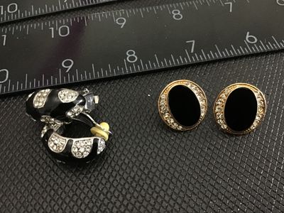 Sale Photo Thumbnail #164: Lot of 2 pairs of vintage clip-on earrings. Includes one pair of silver-tone hoop-style clip earrings with black enamel and clear rhinestone accents, and one pair of gold-tone oval clip earrings featuring black cabochons or enamel centers surrounded by cl