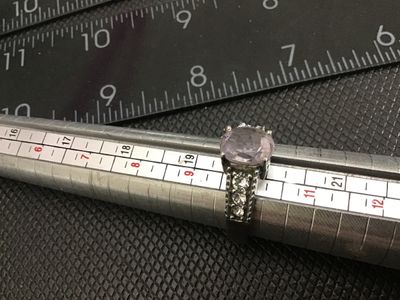 Sale Photo Thumbnail #165: Stainless steel ring featuring a central light purple oval-cut stone flanked by clear accent stones down the shoulders. Marked '316L SS' on the interior band. Ring measures approximately size 9 on the mandrel. Good condition with light surface wear.