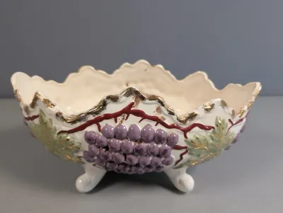 Sale Photo Thumbnail #214: Vintage footed ceramic dish featuring molded grape clusters and leaves with gilt-accented scalloped rim.