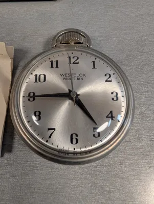 Sale Photo Thumbnail #314: Vintage Westclox Pocket Ben mechanical pocket watch featuring a brushed metallic dial with bold Arabic numerals and a silver-tone case.