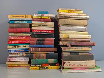 Sale Photo Thumbnail #262: Large collection of vintage hardcover and paperback books arranged in three tall stacks, featuring various fiction and non-fiction titles from the mid-to-late 20th century.