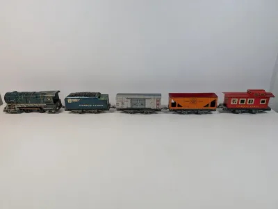 Sale Photo Thumbnail #115: Vintage Unique Art Unique Lines tin litho O-gauge train set, featuring a steam locomotive, coal tender, boxcar, hopper, and caboose.
