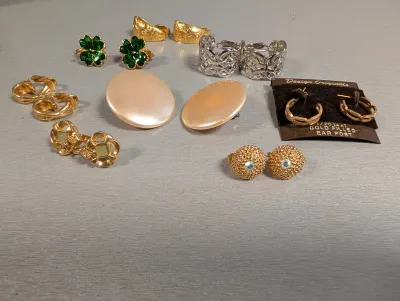 Sale Photo Thumbnail #400: Collection of vintage costume earrings featuring gold-tone clip-ons, enamel four-leaf clovers, faux pearl discs, textured hoops, and a NIB pair by Design Originals.
