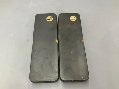 Sale Photo Thumbnail #355: Pair of vintage black hard-shell pistol or firearm cases featuring gold logo emblems and brass latches.