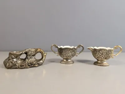 Sale Photo Thumbnail #184: Vintage ornate floral silver-plated tabletop set, including a dual candlestick holder alongside a matching miniature creamer and sugar bowl set with ceramic interiors.