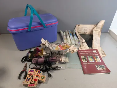 Sale Photo Thumbnail #47: Collection of crafting supplies including a purple plastic tote box, heat gun, soldering iron, rubber stamps, stained glass materials, and pattern books.