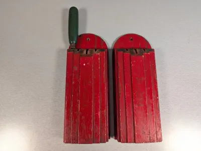 Sale Photo Thumbnail #198: Pair of vintage red painted wooden knife blocks, one featuring a green handle attachment, displaying age-appropriate paint wear and chipping.
