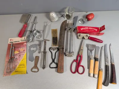Sale Photo Thumbnail #249: Collection of vintage kitchen utensils, including a Krazee-Kutter spiral slicer in its original box, a butcher knife, bottle openers, whisks, and various specialty prep tools.