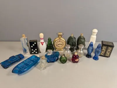 Sale Photo Thumbnail #303: Vintage Avon novelty cologne and perfume bottles, including glass figures shaped like a car, boat, bowling pin, dice, and pocket watch.