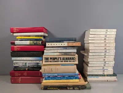 Sale Photo Thumbnail #281: Large collection of hardcover and paperback books organized in three tall stacks, including religious texts, reference books, and popular fiction.