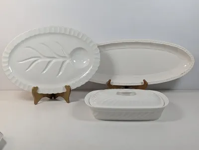 Sale Photo Thumbnail #497: Collection of white ceramic serving pieces, including a tree-and-well platter, an elongated oval fish platter, and a covered rectangular casserole dish.