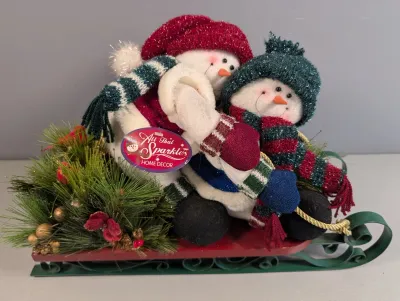 Sale Photo Thumbnail #29: All That Sparkles Home Decor plush snowman pair riding a metal sleigh tabletop decoration, featuring fabric hats, scarves, and faux pine greenery.