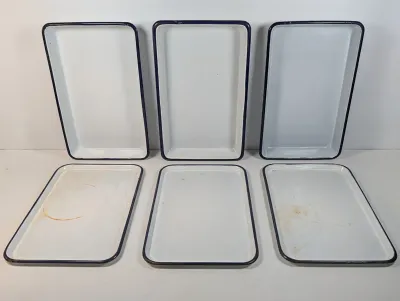Sale Photo Thumbnail #133: Set of six vintage white enamel trays with dark blue trim, showing minor rust and wear consistent with age.