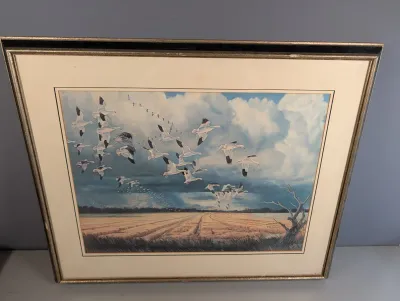 Sale Photo Thumbnail #24: Framed wildlife art print depicting a flock of geese in flight over a rural landscape, housed in a double mat and metallic frame.