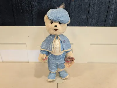Sale Photo Thumbnail #478: Dressed teddy bear collectible figure wearing a light blue velvet outfit with a matching cap and cape.