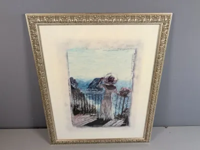Sale Photo Thumbnail #454: Framed impressionist-style art print depicting a woman in a white dress and sunhat overlooking a coastal sea view, set in an ornate silver-finished molded frame.