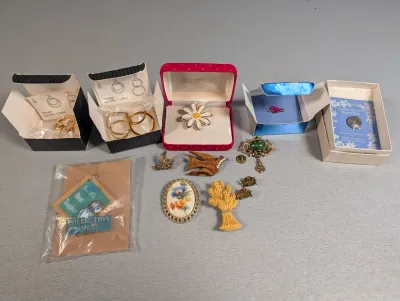Sale Photo Thumbnail #402: Collection of vintage costume jewelry, brooches, and pins, including enamel, wooden bird motifs, floral cameo designs, and boxed pieces.