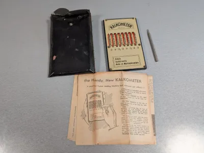 Sale Photo Thumbnail #396: Vintage Kalkometer mechanical pocket adding machine set, including stylus, worn black case, and original instruction booklet.