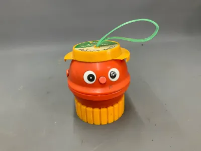 Sale Photo Thumbnail #332: Vintage Child Guidance Melody "Mike" plastic toy, featuring an orange character head with a yellow hat, base, and green plastic loop.