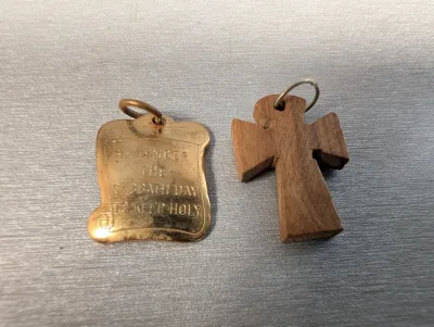 Sale Photo Thumbnail #401: Pair of religious pendants, including a brass scroll-shaped charm inscribed with "Remember the Sabbath Day to Keep Holy" and a carved wooden cross charm.