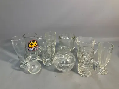 Sale Photo Thumbnail #66: Collection of assorted clear glassware, including beer mugs, small pitchers, a rounded vase, and pilsner-style glasses.