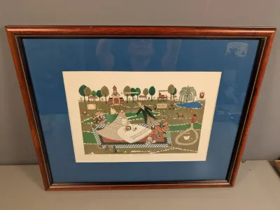 Sale Photo Thumbnail #423: Framed folk art print depicting a whimsical wedding picnic scene, housed in a cherry-finish wood frame with a dark blue mat.