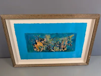 Sale Photo Thumbnail #446: Framed mixed-media 3D assemblage artwork featuring an oceanic theme with shells, netting, and coral elements on a vivid blue background, housed in a wood grain frame.