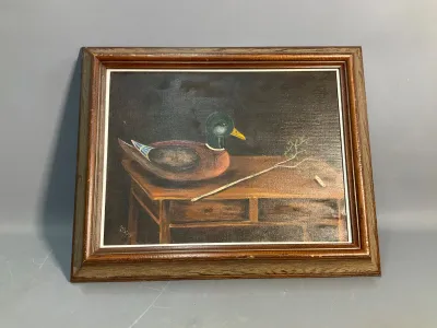 Sale Photo Thumbnail #170: Framed folk art oil painting depicting a duck decoy on a wooden table, signed by the artist in the lower corner and presented in a molded wood frame.