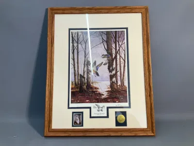 Sale Photo Thumbnail #81: Framed and matted wildlife art print titled 'Twisting Through - Wood Ducks' by Bill Pendergrass, featuring a wood duck stamp and gold medallion inside an oak wood frame.
