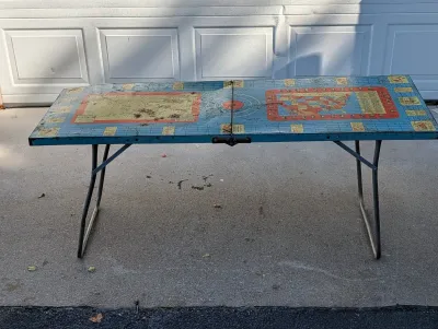 Sale Photo Thumbnail #114: Vintage metal folding table featuring colorful lithographed map graphics on the tabletop, showing age-appropriate wear and surface rust.