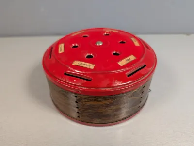 Sale Photo Thumbnail #244: Vintage mid-century round budget bank tin with a red top featuring coin slots labeled for household expenses like Rent and Clothing.