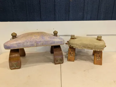 Sale Photo Thumbnail #486: Pair of vintage camel-style footstools featuring wooden bases with brass hardware and worn vinyl and leather cushions.