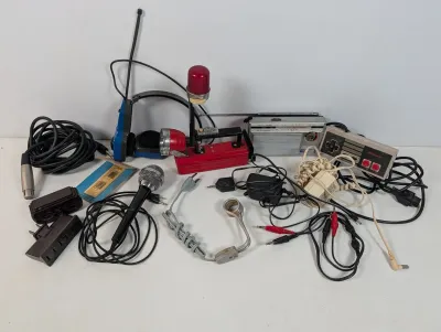 Sale Photo Thumbnail #107: Assorted vintage electronics and accessories, including a handheld microphone, NES controller, portable transistor radio, battery-operated emergency light, and various audio cables.