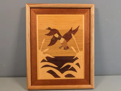 Sale Photo Thumbnail #457: Framed wood marquetry wall art depicting ducks flying over a wetland, composed of contrasting natural wood veneers.