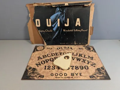 Sale Photo Thumbnail #279: Vintage William Fuld Ouija board set, including the game board, plastic planchette, and damaged original box.