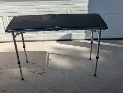 Sale Photo Thumbnail #111: Portable folding utility table with an aluminum frame, black surface, and adjustable height legs.