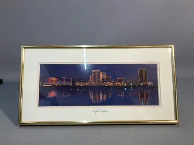 Sale Photo Thumbnail #160: Framed panoramic photograph of the Norfolk, Virginia skyline at night, housed in a thin gold metal frame with a double mat.