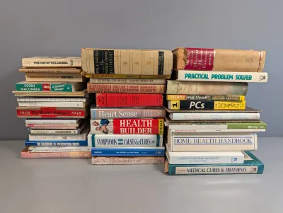 Sale Photo Thumbnail #272: Large assortment of vintage and modern hardcover and paperback books organized in three neat stacks. Topics include medical references, home health handbooks, religious texts, and general fiction.