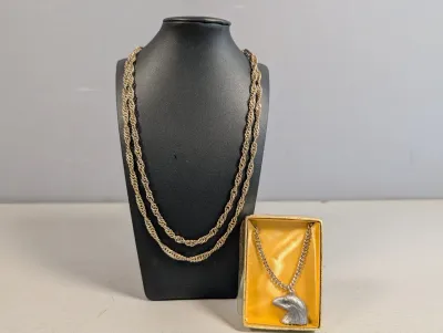 Sale Photo Thumbnail #404: Gold-tone rope chain necklace draped on a black bust display, paired with a boxed silver-tone chain featuring a eagle head pendant.