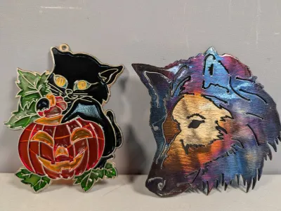Sale Photo Thumbnail #410: Two decorative suncatchers, including a stained glass-style black cat on a jack-o'-lantern and a heat-patinated metal wolf head cutout.