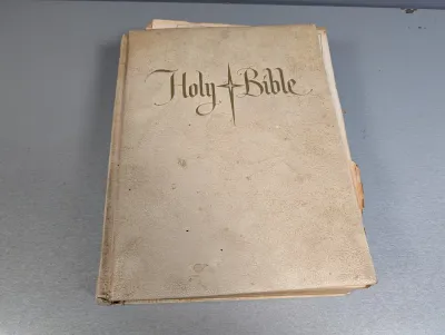 Sale Photo Thumbnail #264: Vintage off-white textured hardcover Holy Bible with stylized gold lettering and star motif on the front cover, showing light wear and age toning.