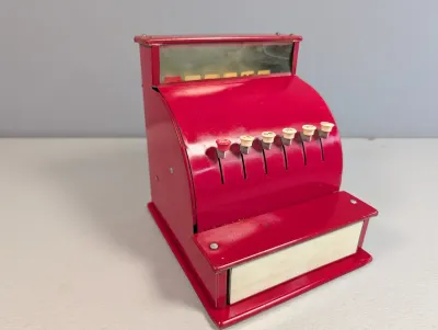 Sale Photo Thumbnail #217: Vintage red metal toy cash register with white plastic key buttons and pull-out drawer, showing light wear.