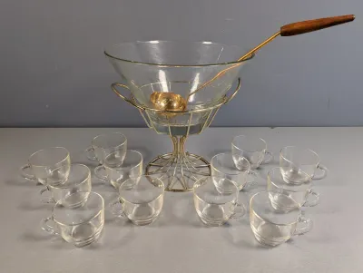 Sale Photo Thumbnail #274: Mid-century modern punch bowl set featuring a conical glass bowl in a brass wire stand, a wooden-handled ladle, and twelve matching glass cups.