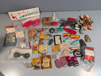 Sale Photo Thumbnail #215: Collection of vintage mid-century novelty items, magic tricks, gag gifts, and small stocking stuffers displayed on a table.