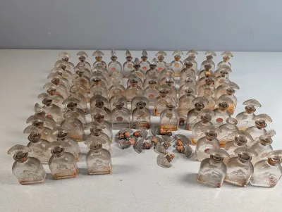 Sale Photo Thumbnail #234: Large collection of miniature clear glass perfume bottles with fan-shaped stoppers and cork necks, showing varying degrees of vintage wear and residue.